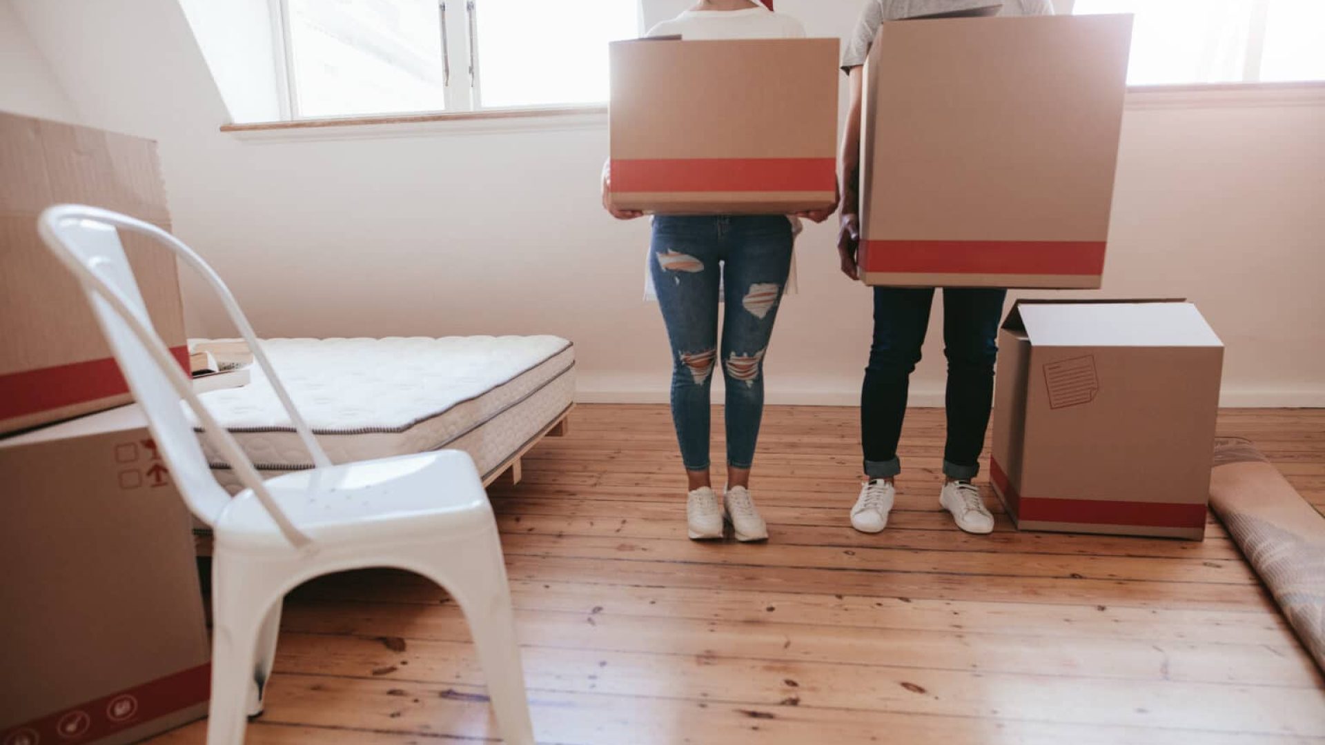 Cropped shot of young couple with big cardboard boxes moving to new place. Man and woman carrying big boxes and moving into new house.